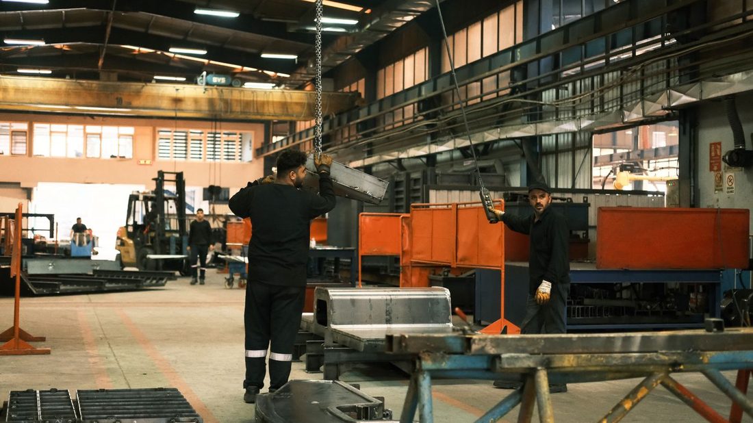 Home 11 Workers moving heavy steel fabrication with an overhead chain hoist